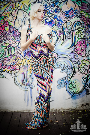 Outdoor portrait of a young woman in a brightly patterned dress against a graffiti wall