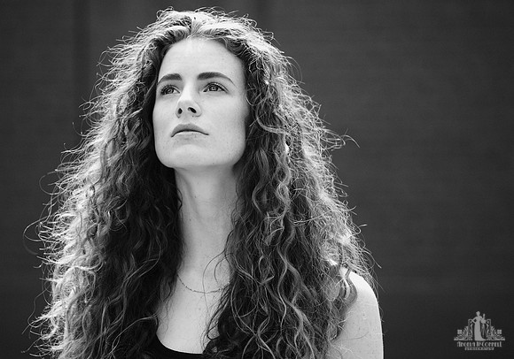 Outdoor portrait of a young woman with long curly hair looking at the sky