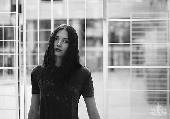 Outdoor black and white portrait of a young woman leaning against a glass wall