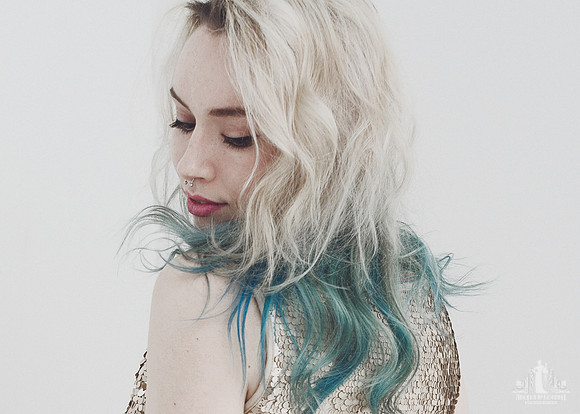 Portrait of a young woman with blonde and blue-green hair looking over her shoulder