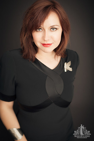 Portrait of a young woman with auburn hair in a black dress and silver bird brooch smiling at the camera