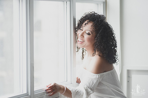 Natural light portrait of a young woman with natural hair looking out the window laughing