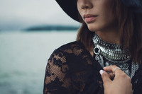 Natural light portrait of a young woman in a black hat and silver necklaces with English Bay in the background at dusk