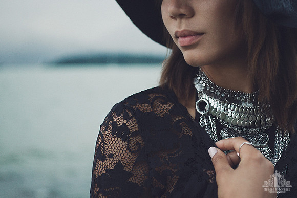 Natural light portrait of a young woman in a black hat and silver necklaces with English Bay in the background at dusk