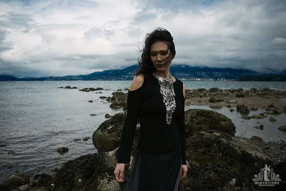 Contemporary environmental portrait of an asian woman standing on a rocks shoreline as the wind sweeps her hair and clothing across her by Vancouver portrait photographer Angela McConnell