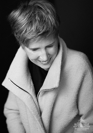Contemporary black and white studio portrait of an older woman in a coat looking down and smiling by Vancouver portrait photographer Angela McConnell