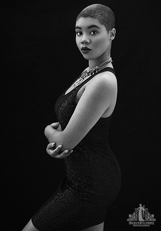 Contemporary black and white studio portrait of a young black woman standing in profile while looking at the camera by Vancouver portrait photographer Angela McConnell