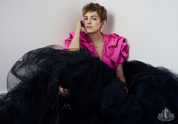 Contemporary natural light studio portrait of a young woman in a full black tulle skirt and pink crop jacket sitting on the floor looking at the camera by Vancouver portrait photographer Angela McConn