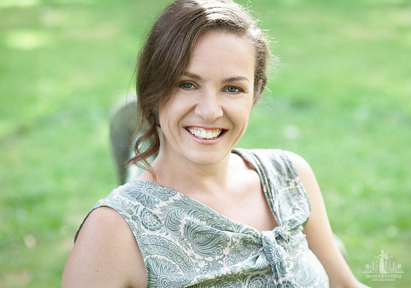 Natural light head shot of a woman in a green shirt sitting on a park bench