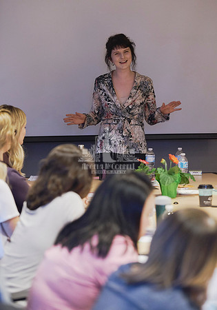 A presenter stands at the head of a board room table surrounded by women during a workshop