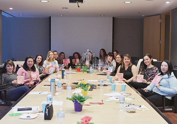A group of women seated around a board room table holding notebooks during a workshop