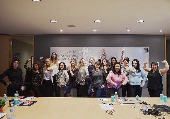 Group of women in front of a white boards with empowering messages in power poses during a workshop