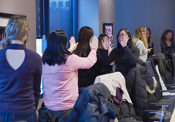 Group of women walking around a boardroom table smiling and giving each other high fives