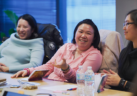 Woman in a pink shirt talking and smiling as she shares with the women sitting around her during a workshop