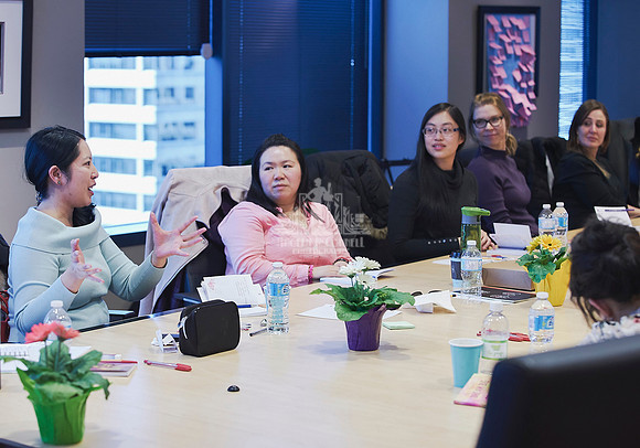 Women sitting at a board room table listening to another woman share during a discussion in a workshop