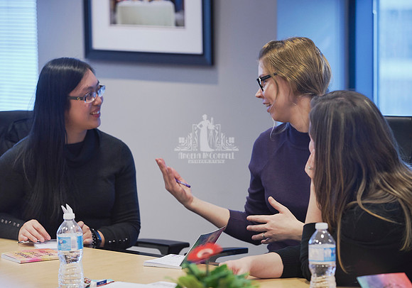 Three women sitting at a board room table discuss with each other during an exercise at a workshop