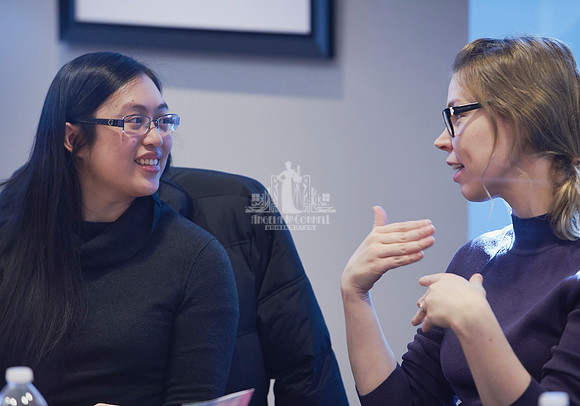 Two women sitting at a board room table discuss with each other during an exercise at a workshop