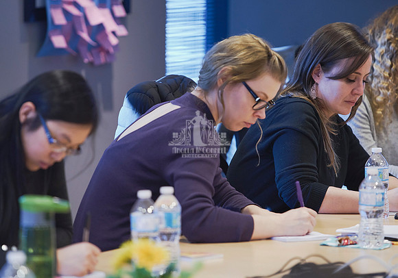 Women sitting at a board room table writing in workbooks during an exercise at a workshop