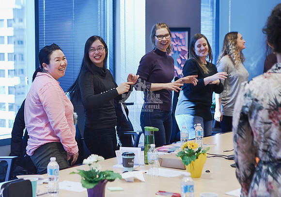 Group of women walking around a boardroom table smiling and giving each other high fives