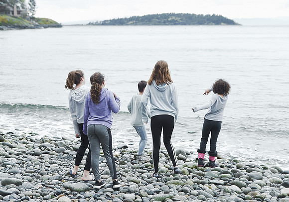 Girls play by the water on a pebble beach at Halfmoon Haven in Sechelt BC