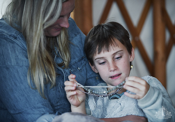 A young girl plays with a necklace while being hugged by her mother  at a mother and daughter workshop by Vancouver workshop and retreat photographer Angela McConnell