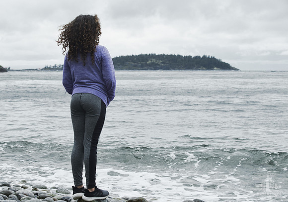A young girls stands looking over the water on a pebble beach at Halfmoon Haven in Sechelt BC