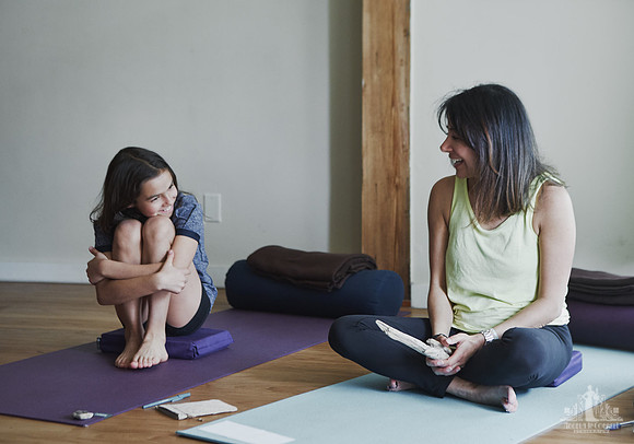 A daughter smiles at her mother as they sit on yoga mats during an exercise at a mother and daughter workshop by Vancouver workshop and retreat photographer Angela McConnell
