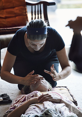 A woman applies a face mask to another woman lying on the ground at a womens' retreat at Halfmoon Haven on the Sunshine Coast, BC by Vancouver workshop and retreat photographer Angela McConnell