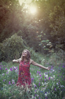 Natural light portrait of a young woman in a field of flower with the sun setting behind her