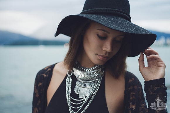 Contemporary natural light portrait of a young woman in a floppy black hat and silver necklaces with West Vancouver and English Bay in the background by Vancouver portrait photographer Angela McConnel